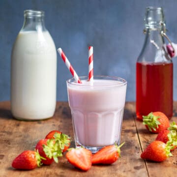 Glass of strawberry milk, bottle of milk and bottle of strawberry syrup, on a wooden table.