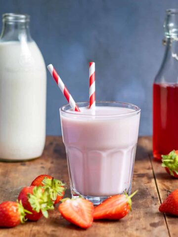 Glass of strawberry milk, bottle of milk and bottle of strawberry syrup, on a wooden table.