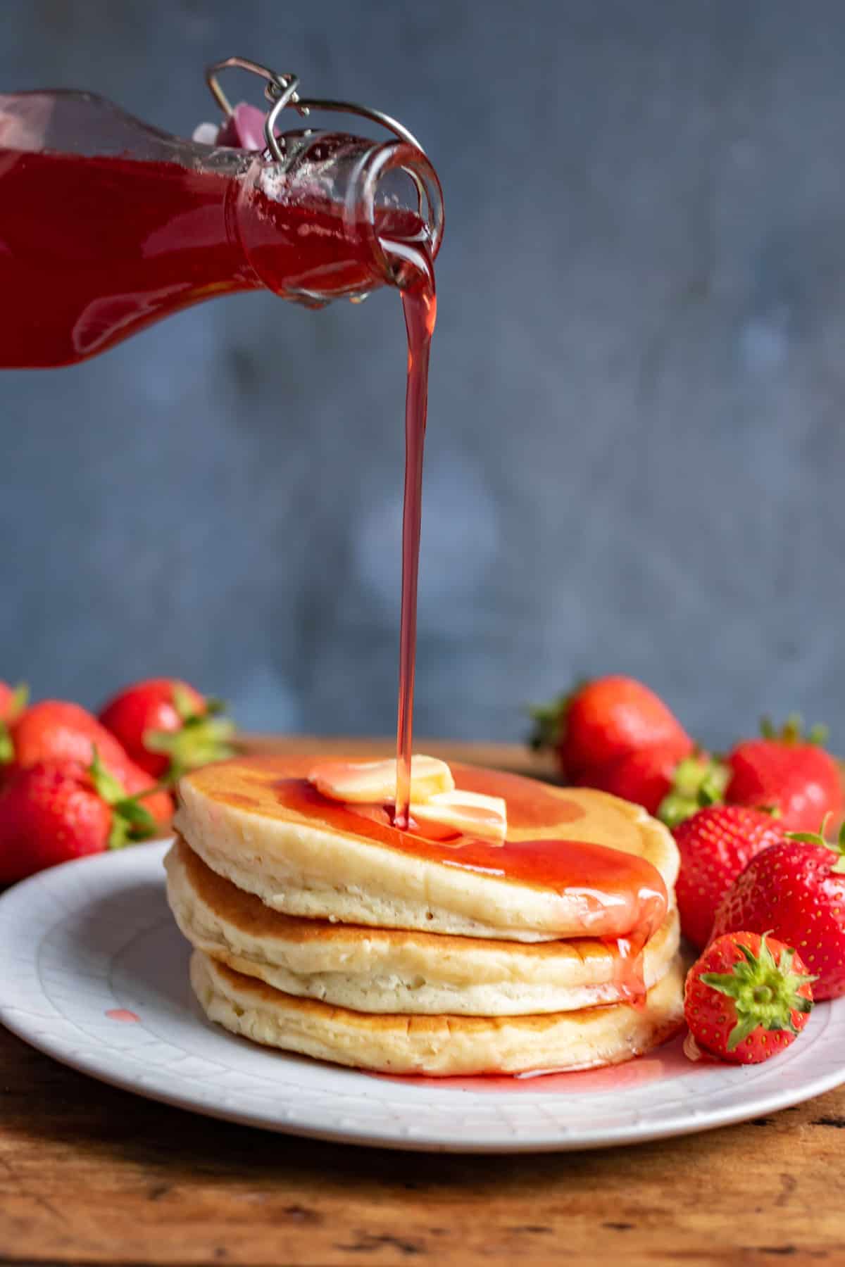 Pouring strawberry syrup onto a stack of pancakes.