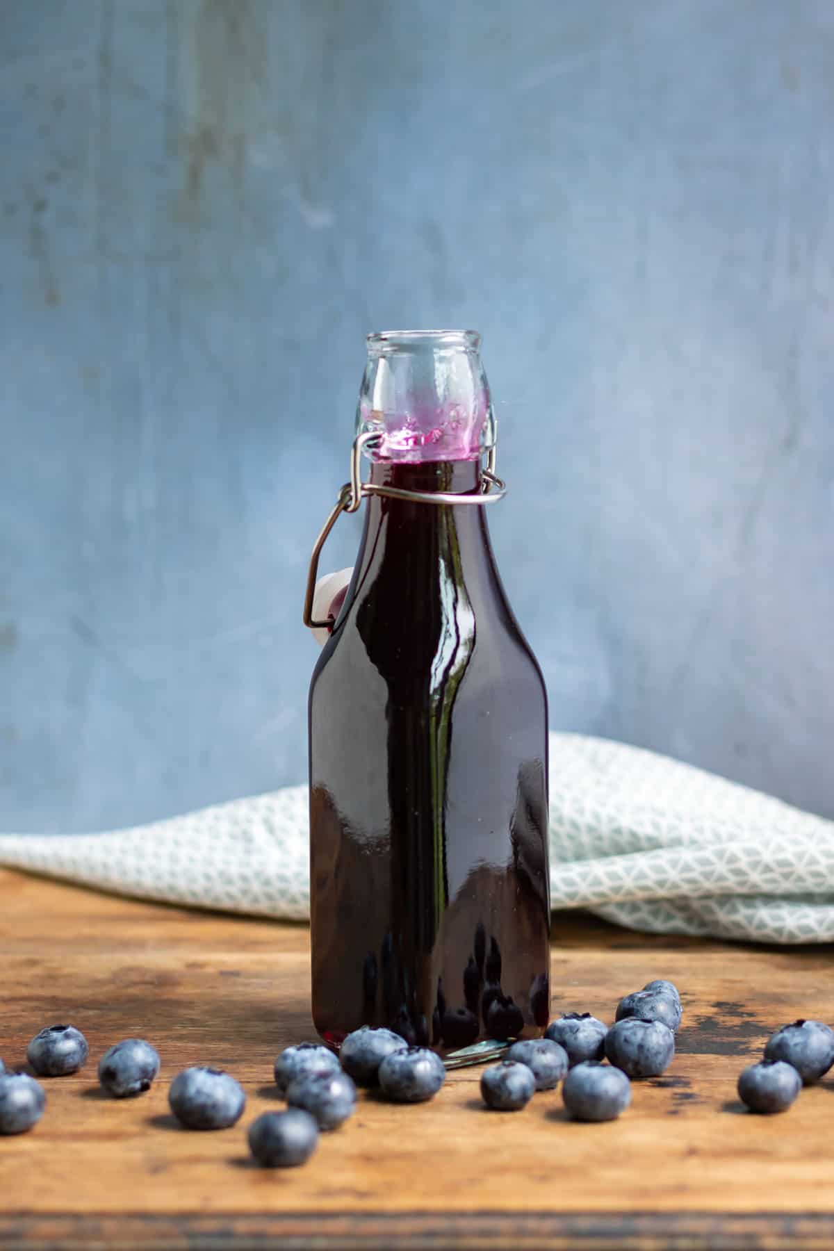 Bottle of syrup in front of blueberries.