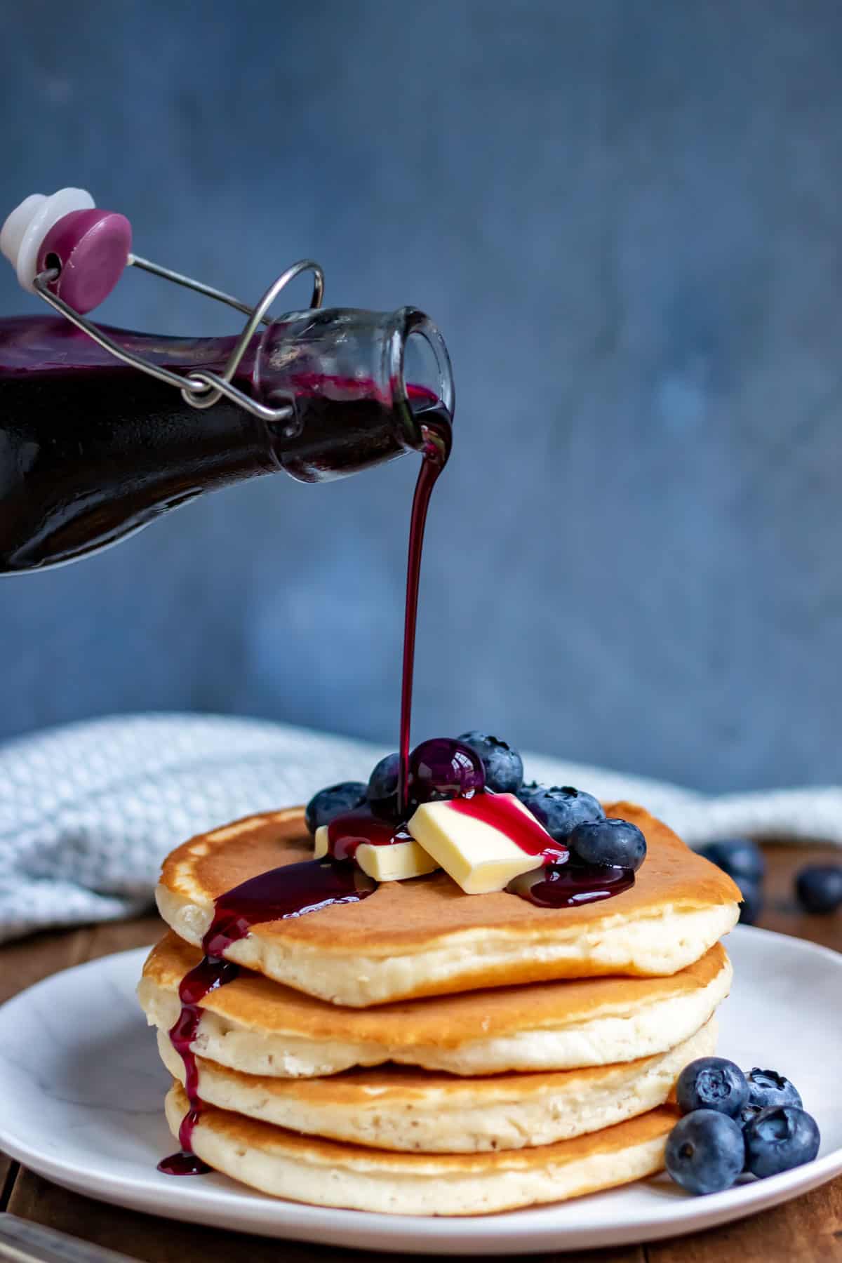 Pouring blueberry syrup onto pancakes.