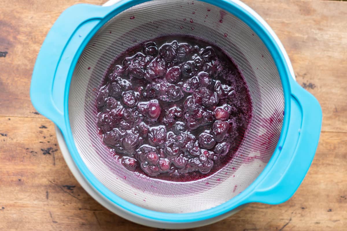 Straining blueberries out of simple syrup.