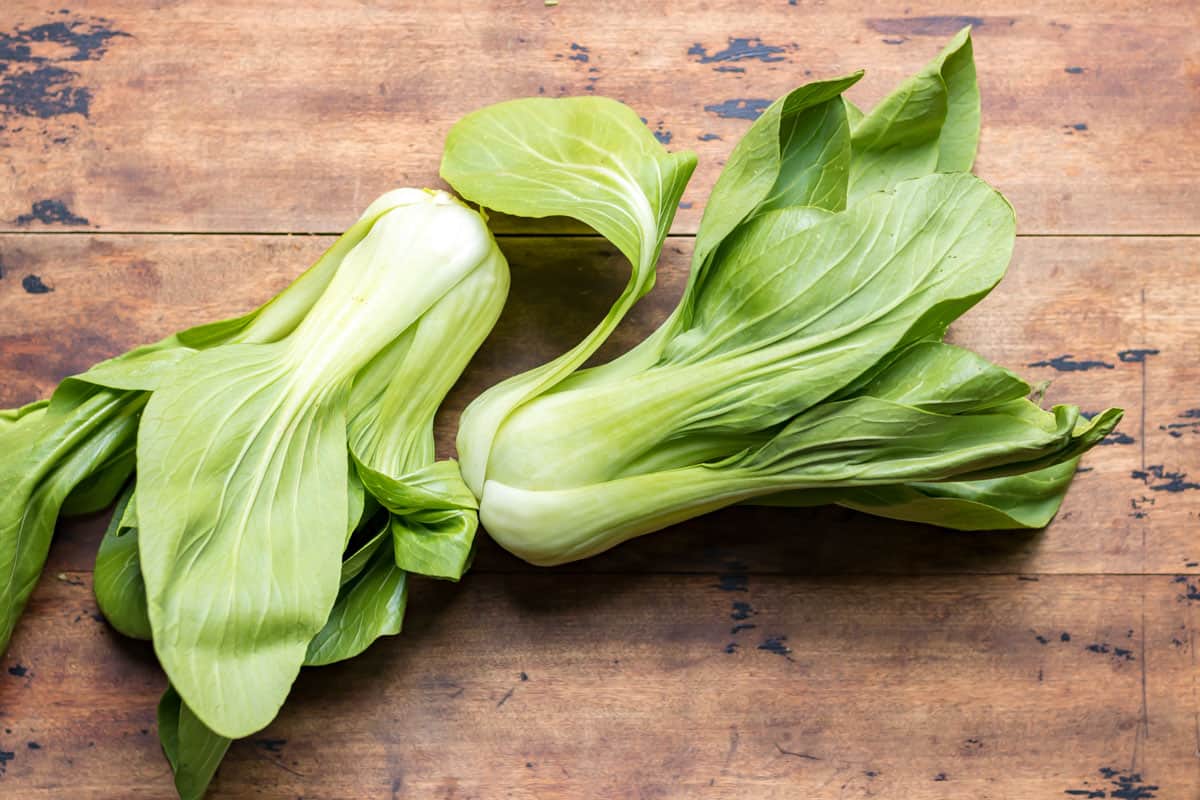 Two bok choi on a wooden table.