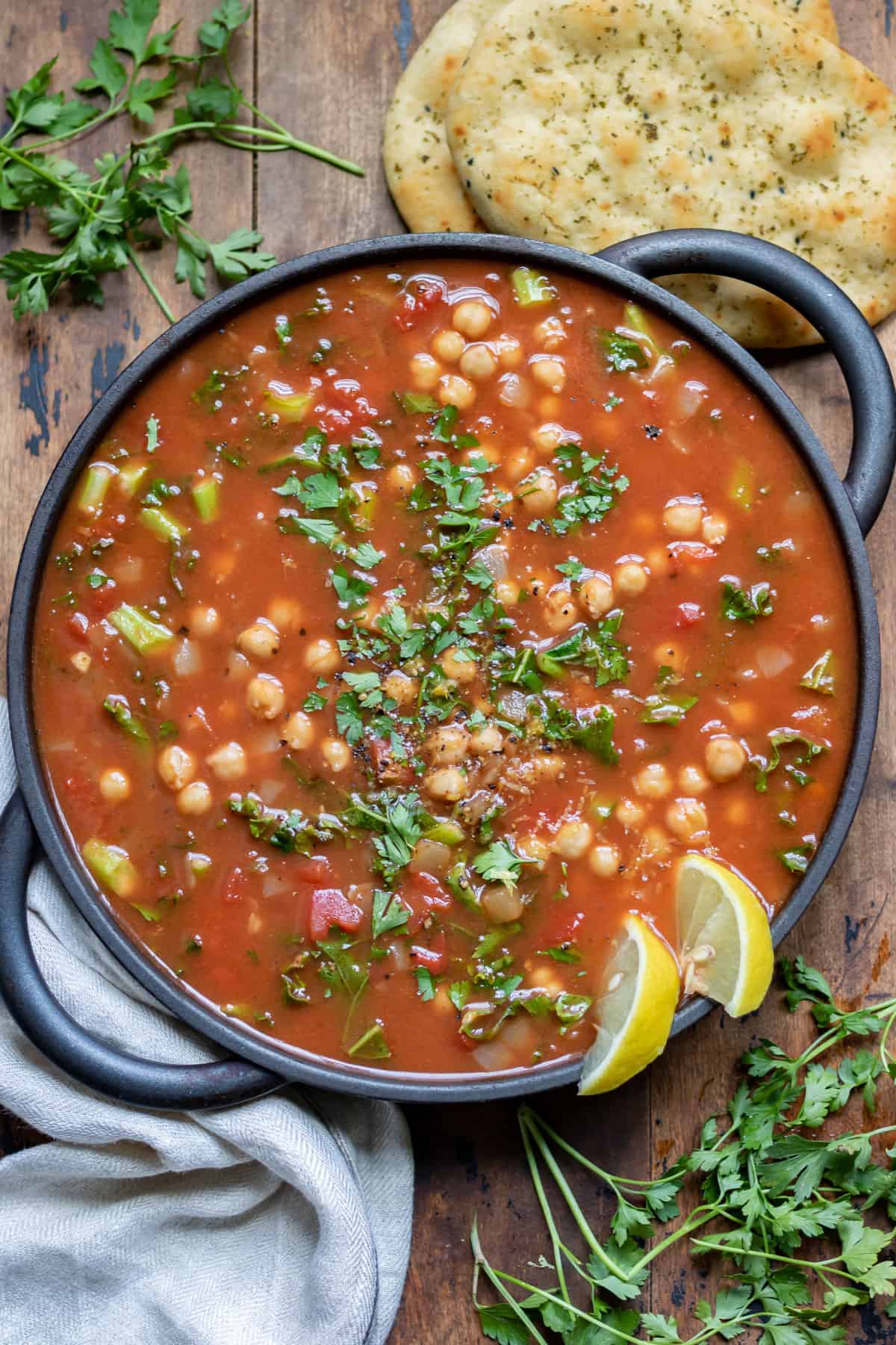 Table with dish of soup, plus flatbreads and herbs.