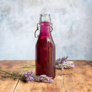 A wooden table with a bottle of lavender simple syrup.