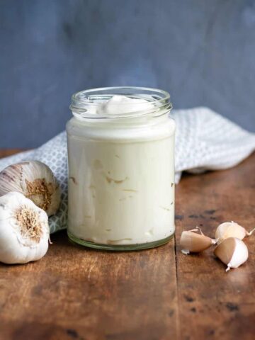 Jar of vegan aioli on a table next to cloves of garlic.