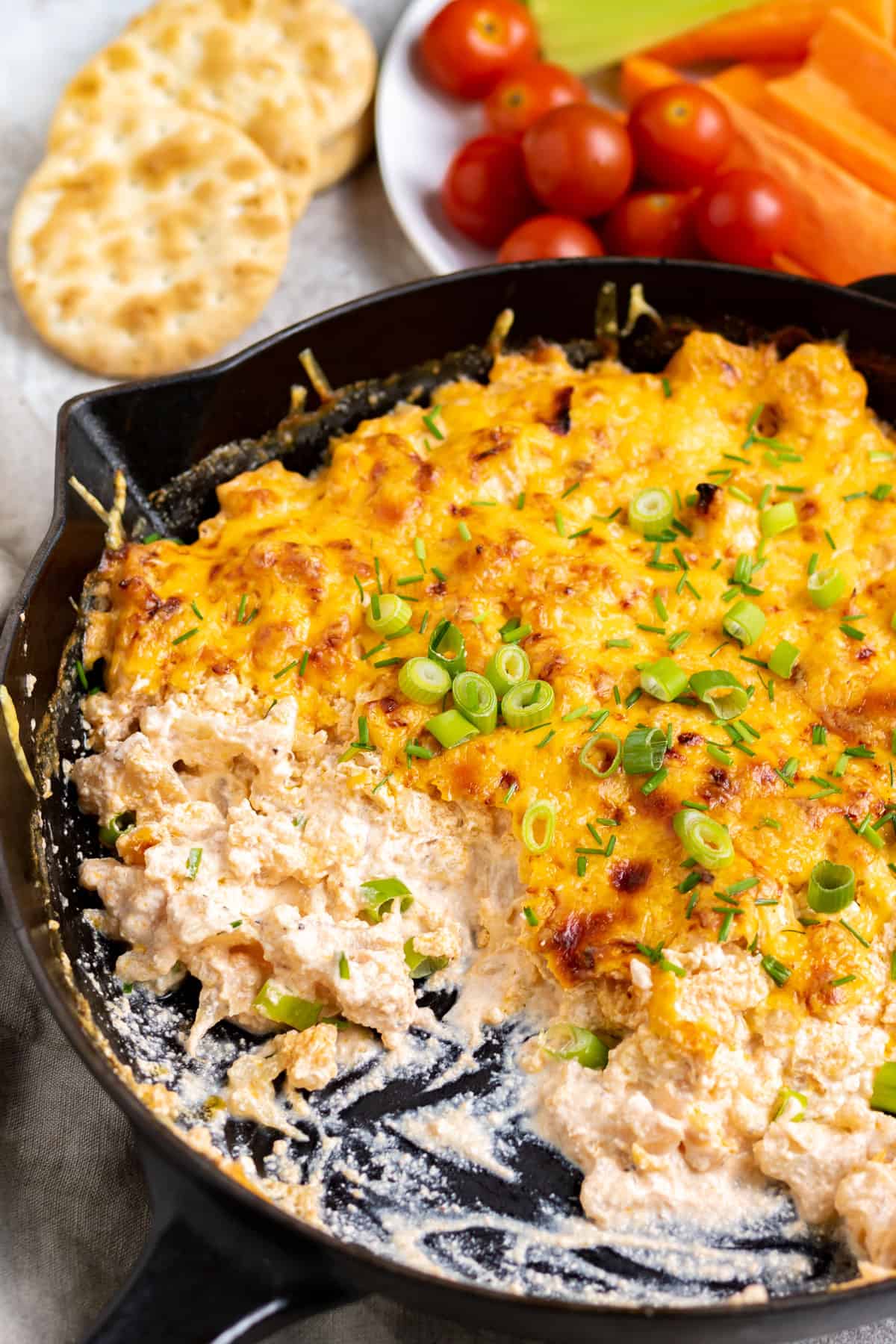 Skillet of buffalo cauliflower dip surrounded by veggies and crackers.
