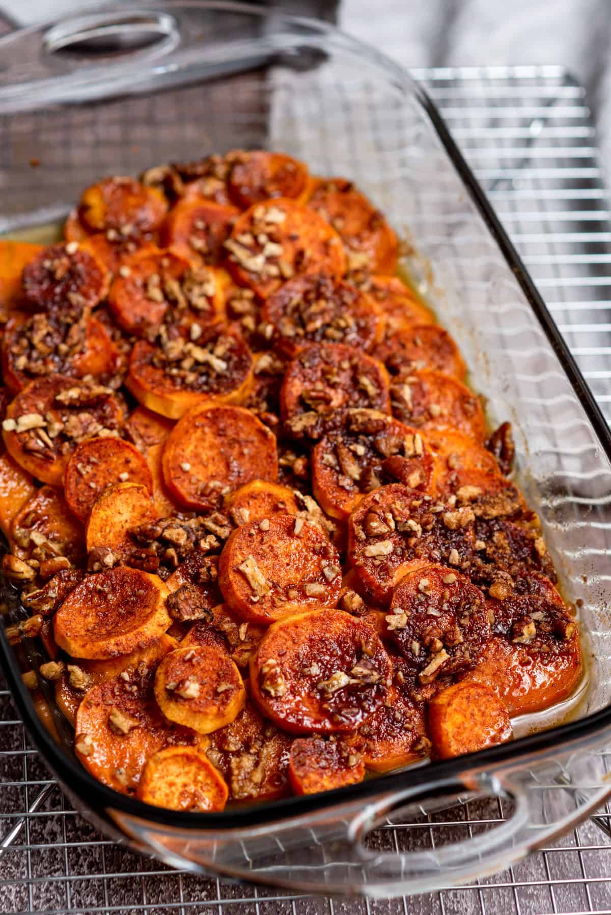 A glass dish with layers of sliced sweet potatoes with a candied pecan topping.