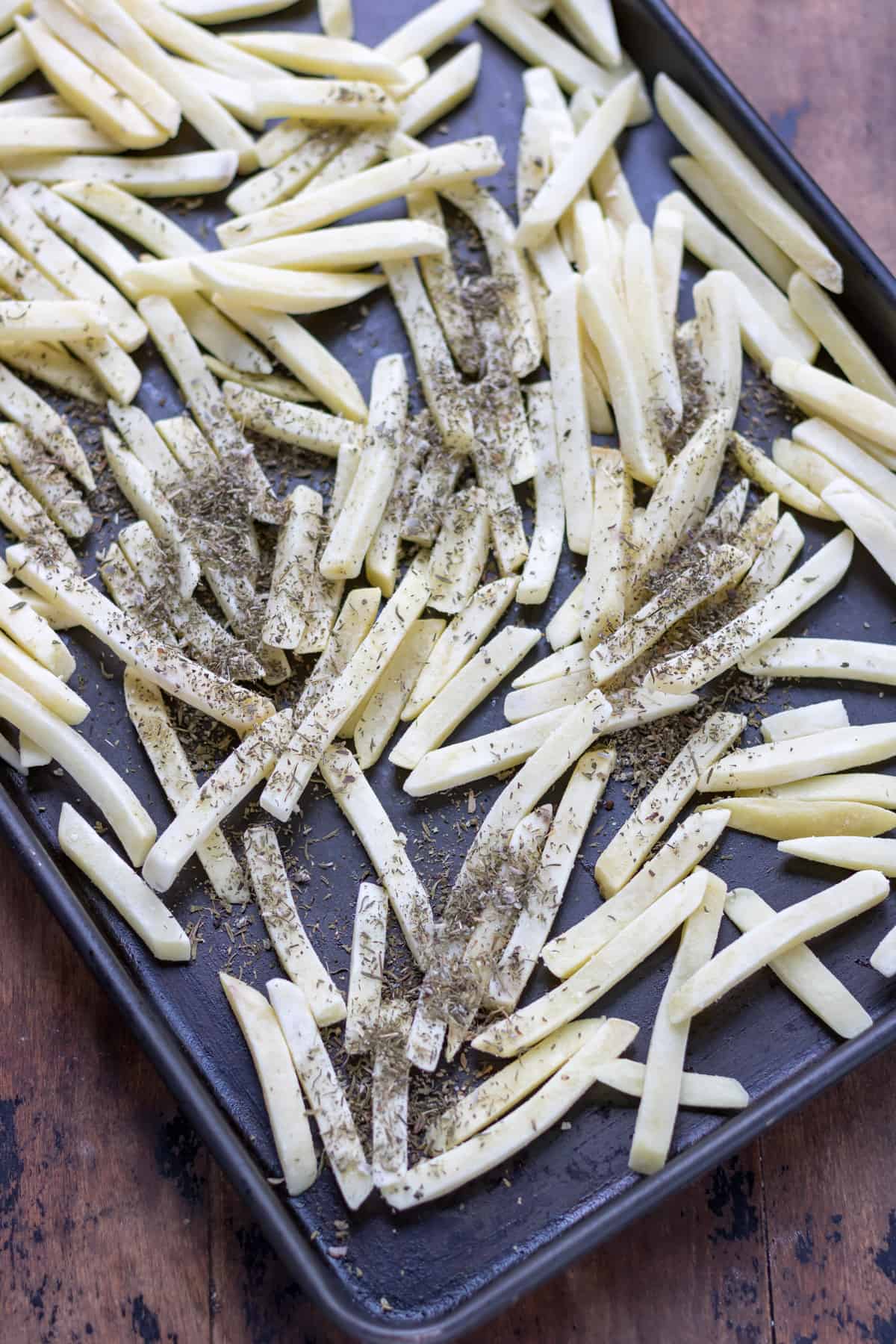 A baking tray of fries seasoned with dried sage, ready to cook.
