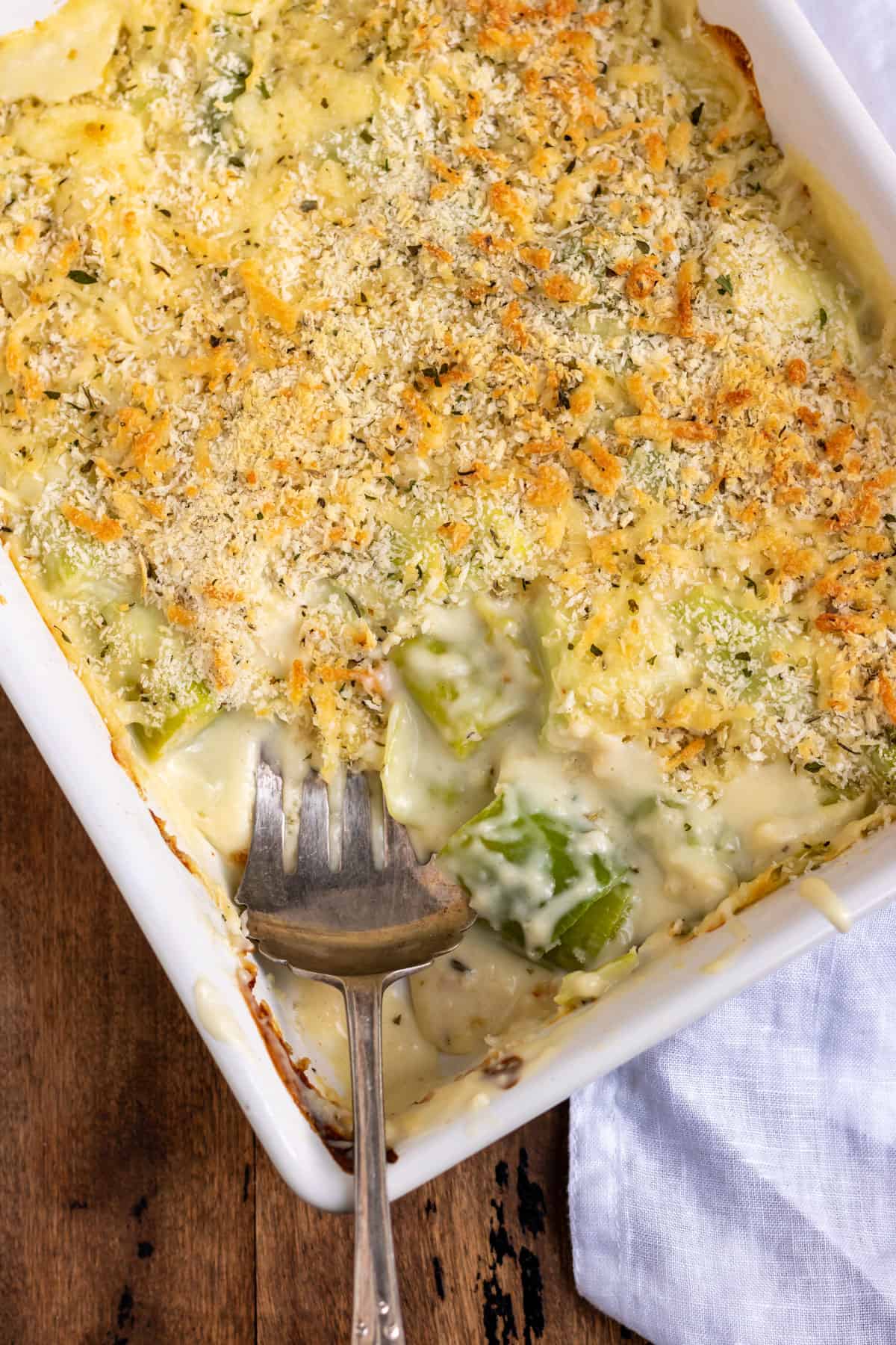 Serving dish of leek gratin, with a portion removed and a serving spoon in it.