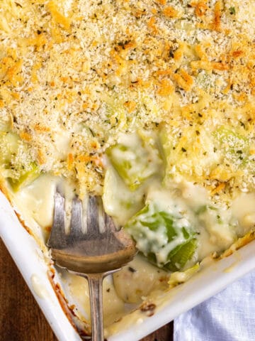 A baking dish of cheesy leeks gratin, with a serving spoon and a portion removed.