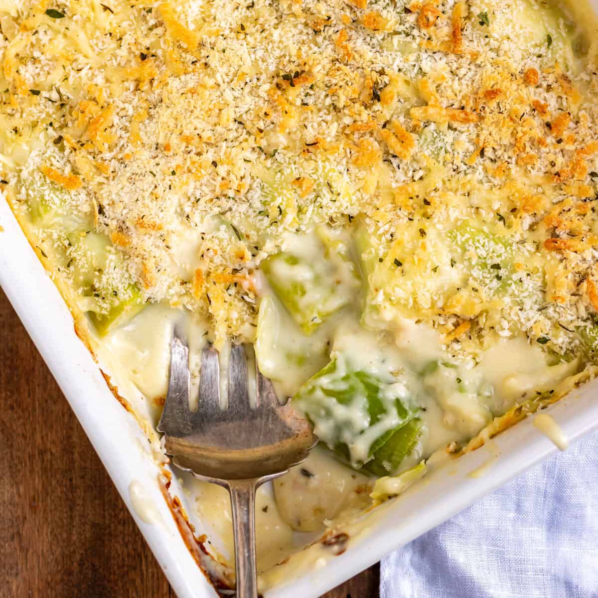 A baking dish of cheesy leeks gratin, with a serving spoon and a portion removed.