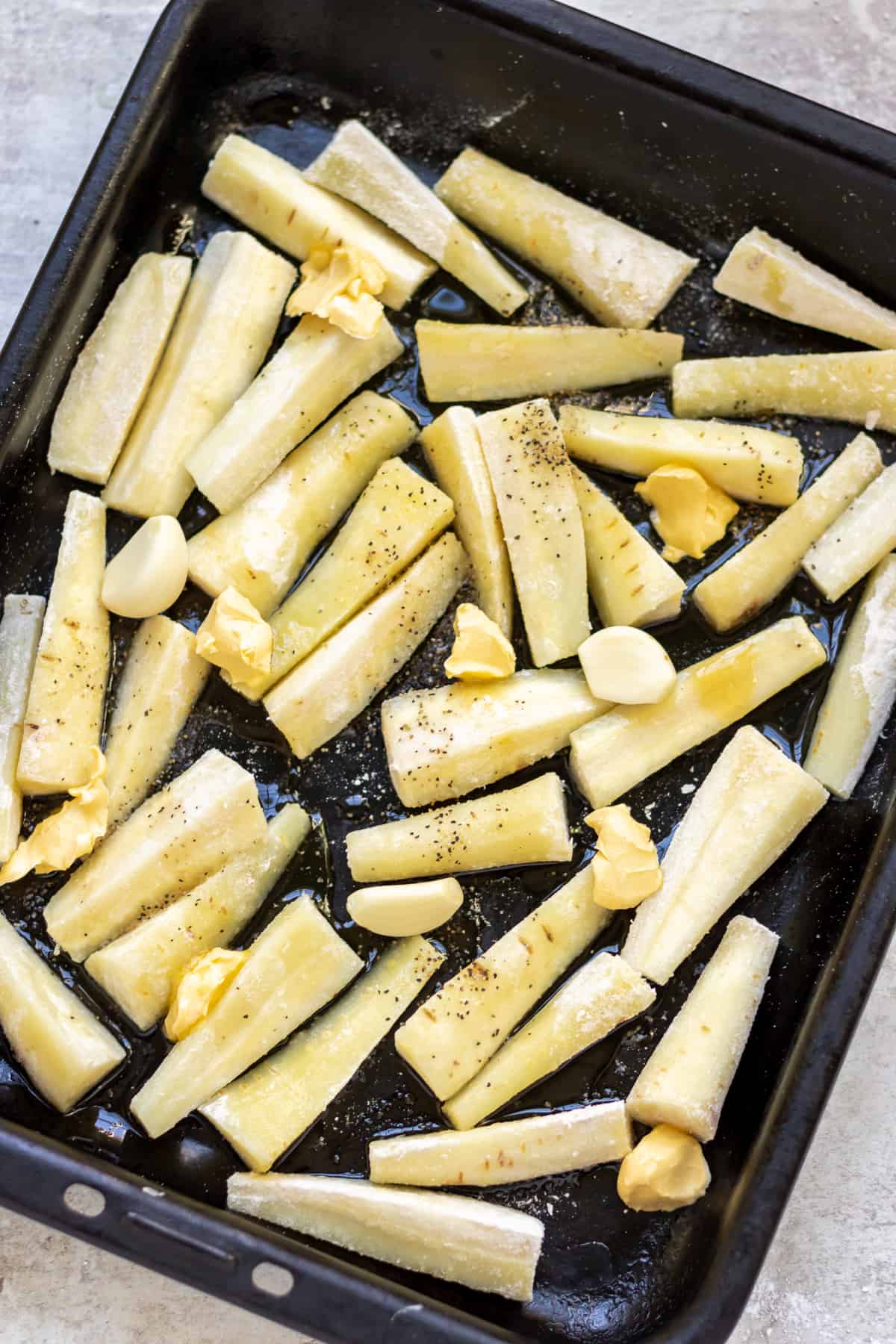Cut parsnips on a roasting tray with seasonings.