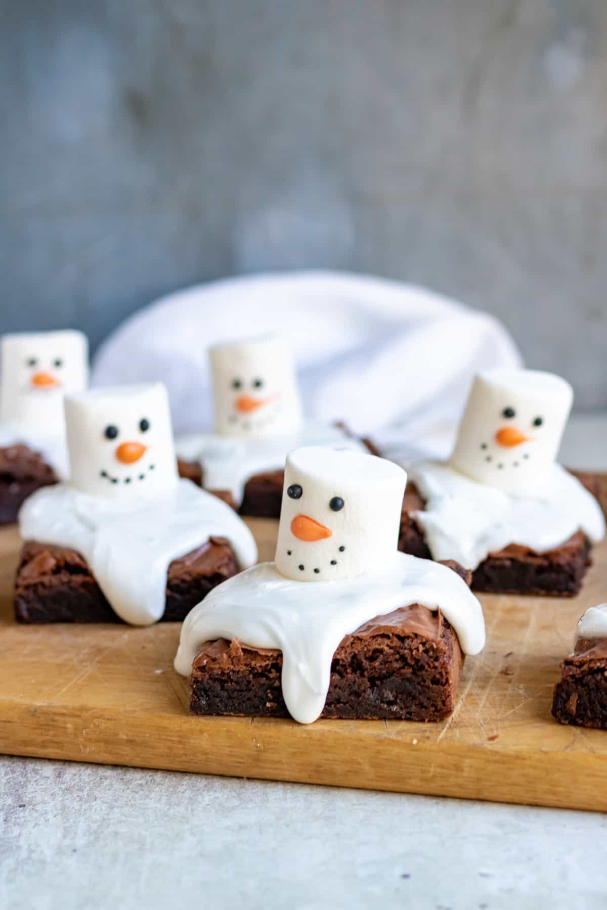 Close up of brownies topped with icing and marshmallows decorated to look like snowmen.