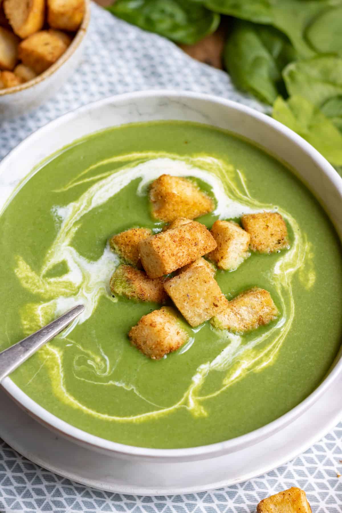 Close up of a bowl of spinach soup swirled with cream and topped with croutons.