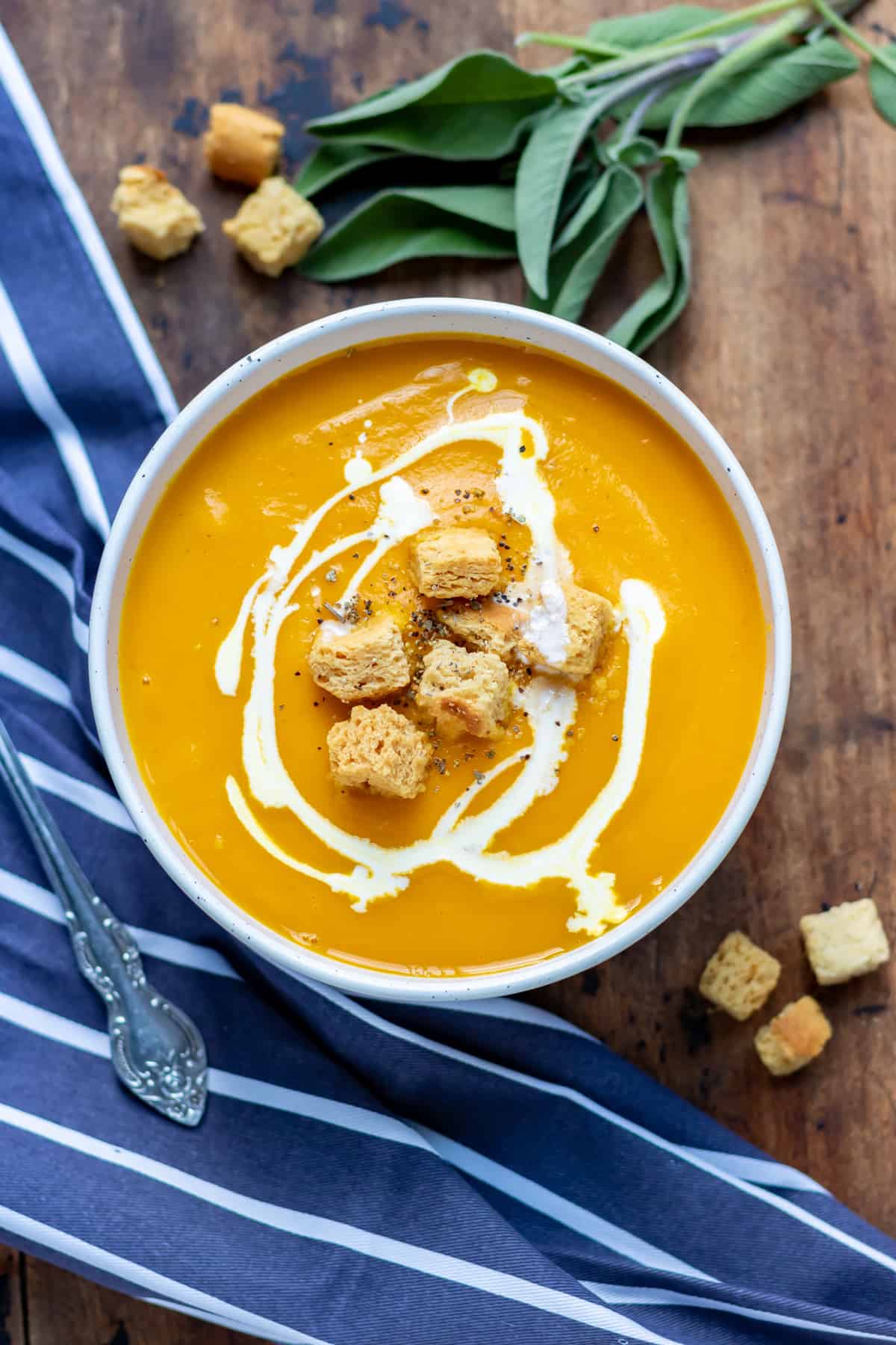 A table with a bowl of butternut squash with swirled cream and croutons.
