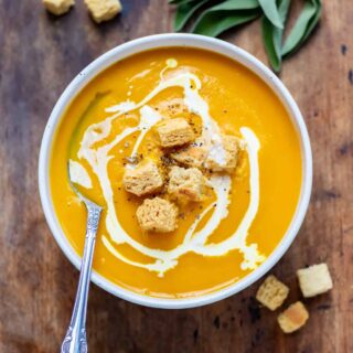 A bowl of soup with a spoon, swirled cream and croutons.