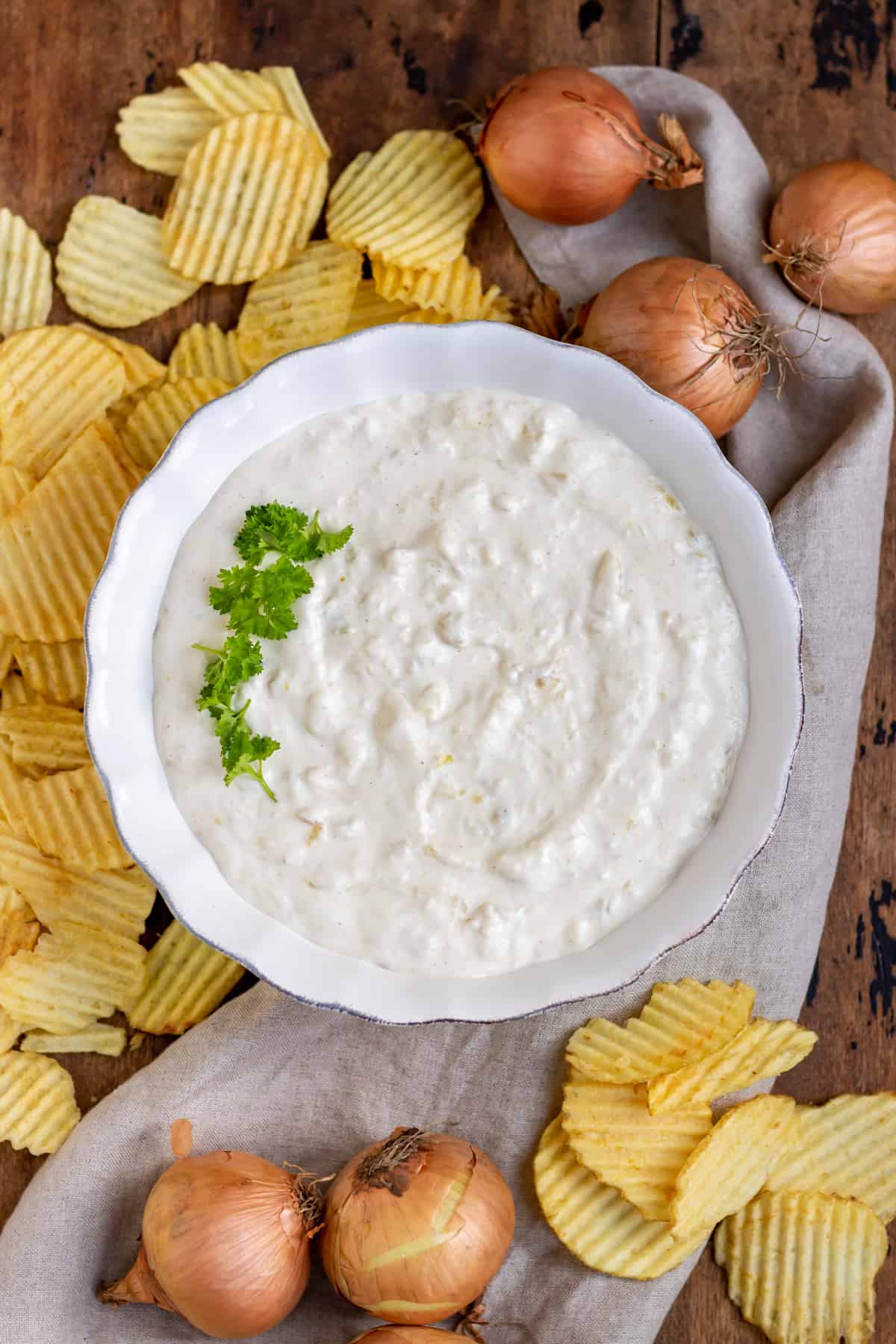 A bowl of french onion dip, surrounded by chips and onions.