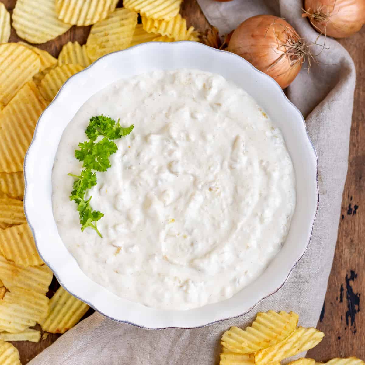 A bowl of french onion dip, surrounded by chips and onions.