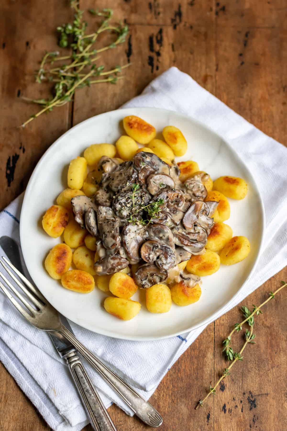 A wooden table with a plate of gnocchi and mushroom sauce.