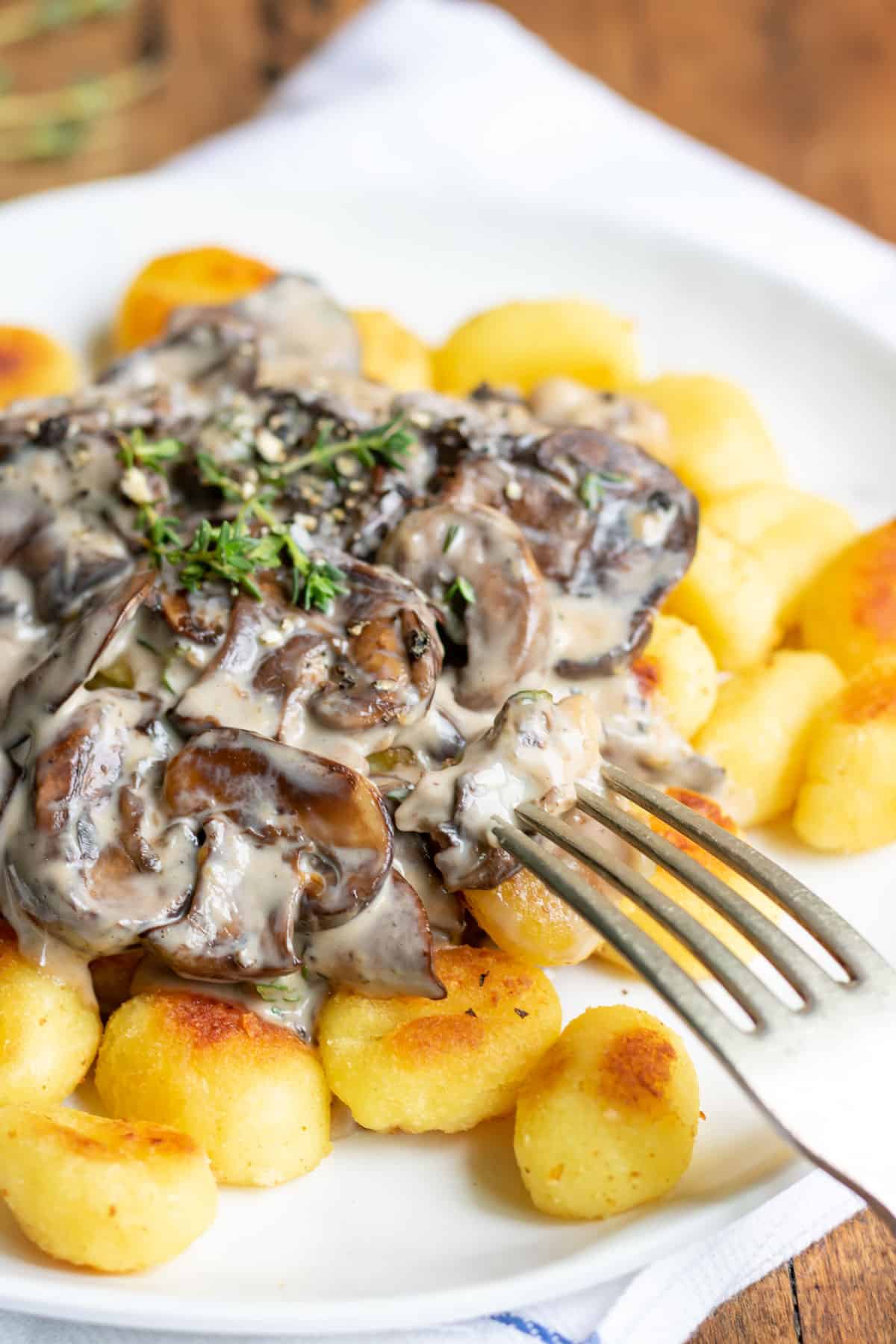 A fork in a plate of gnocchi topped with creamy mushroom sauce.