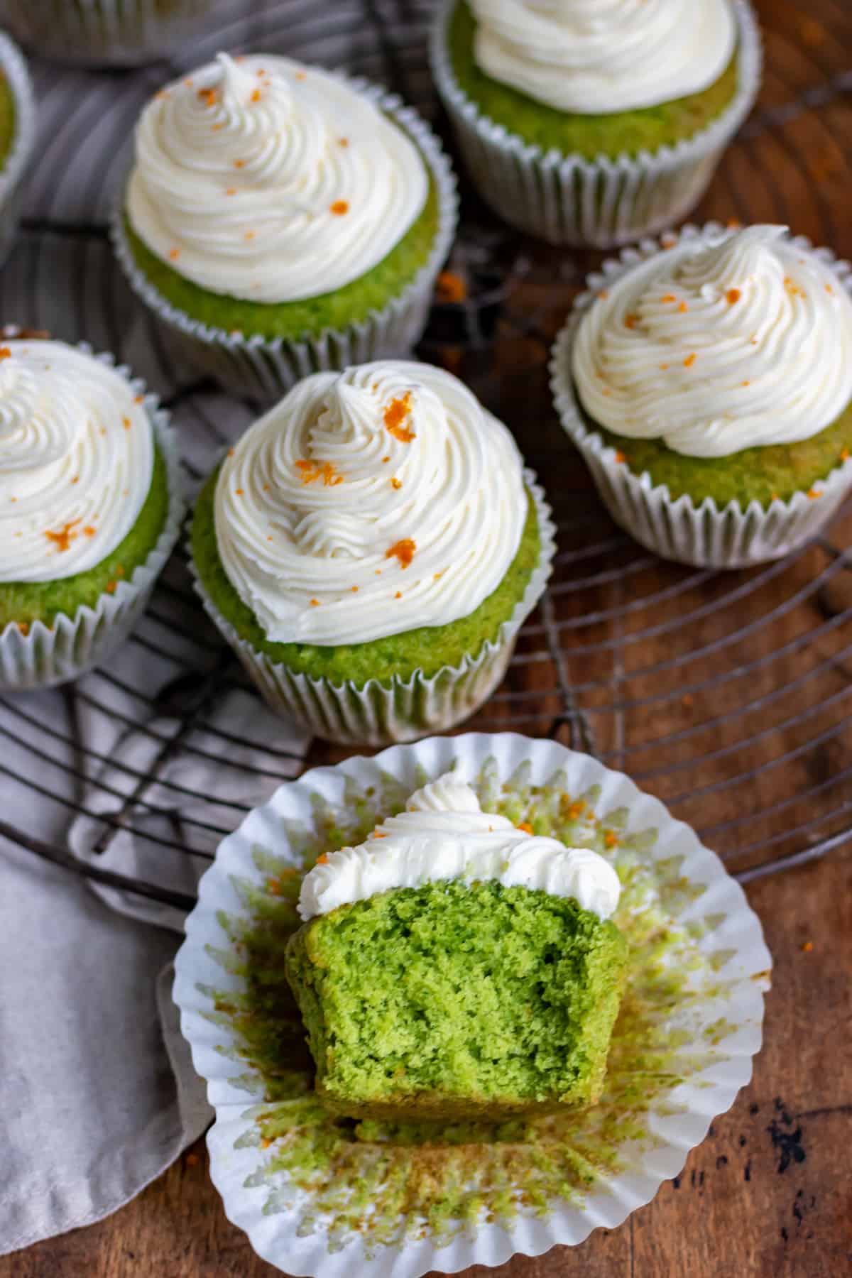 Looking down at a cupcake with a bite out and a cooling rack of frosted kale cupcakes.