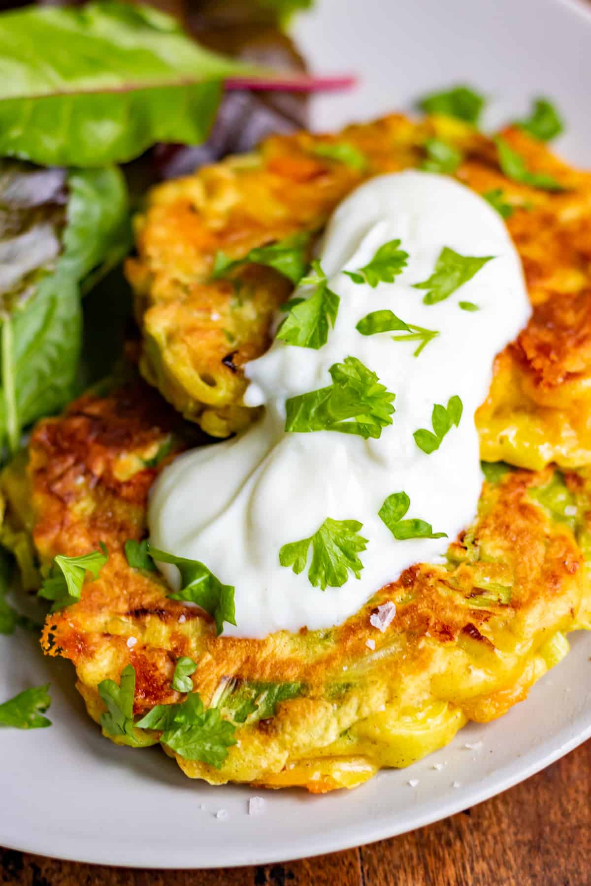 Close up of two leek fritters on a plate with yogurt sauce and salad.
