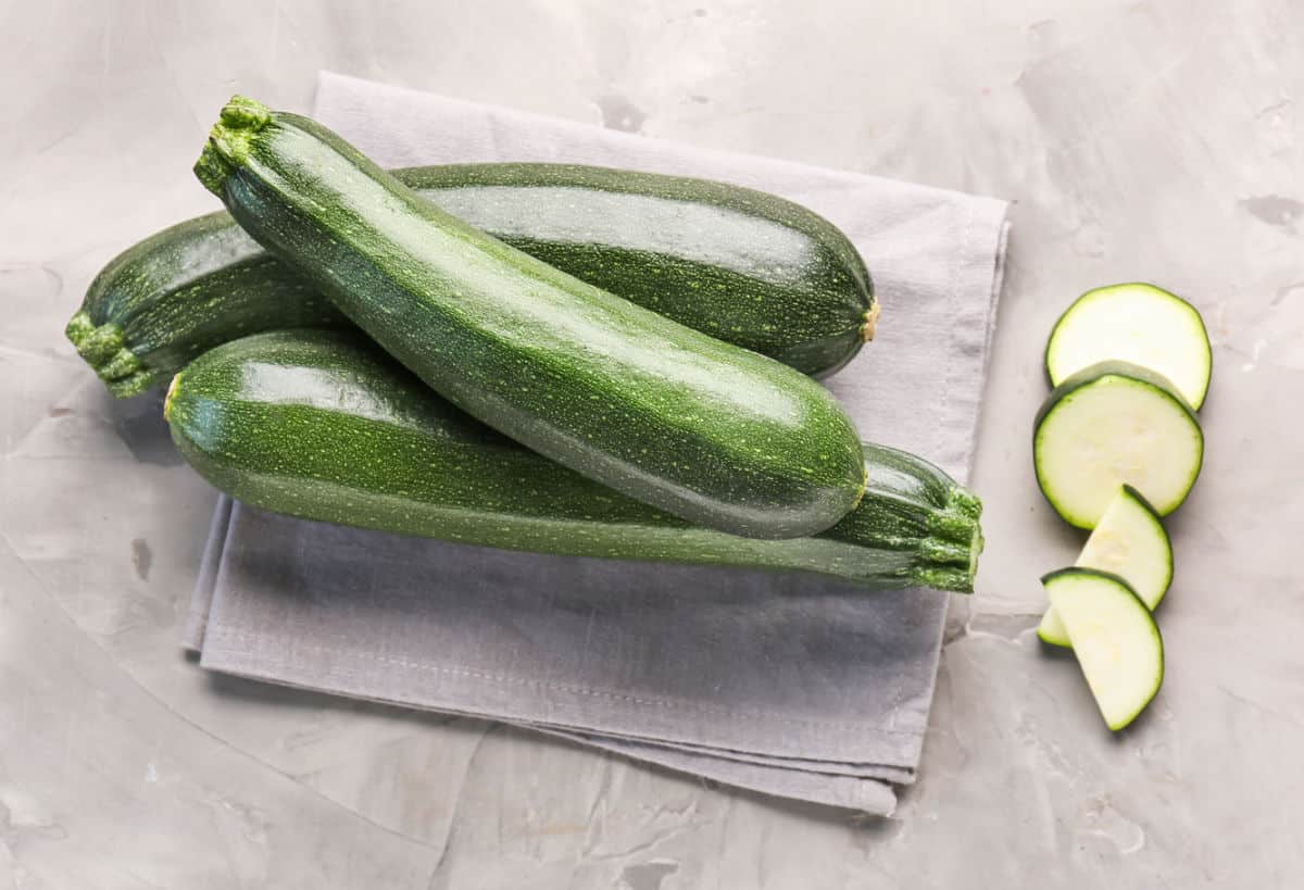 Zucchini (courgette) on a table next to slices.