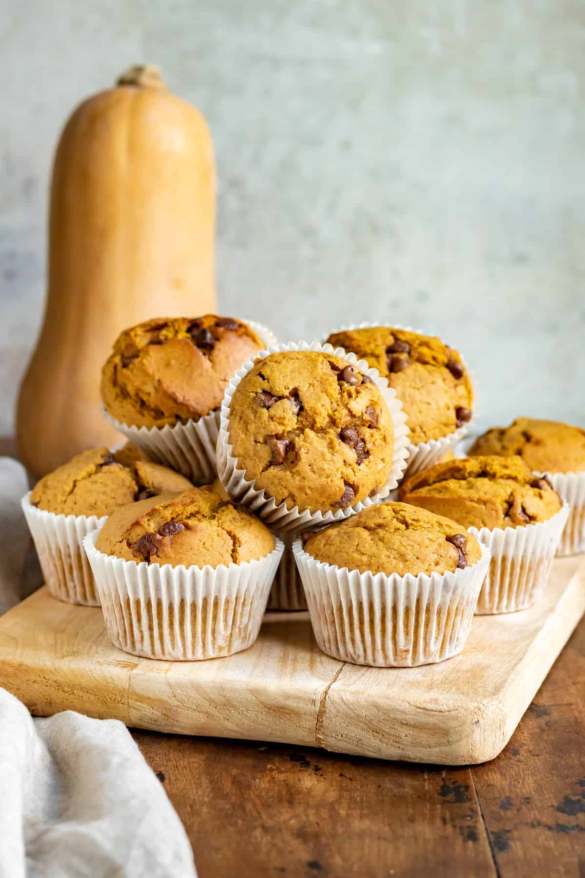 A pile of muffins in front of a butternut squash.