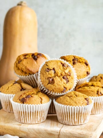 A pile of muffins in front of a butternut squash.