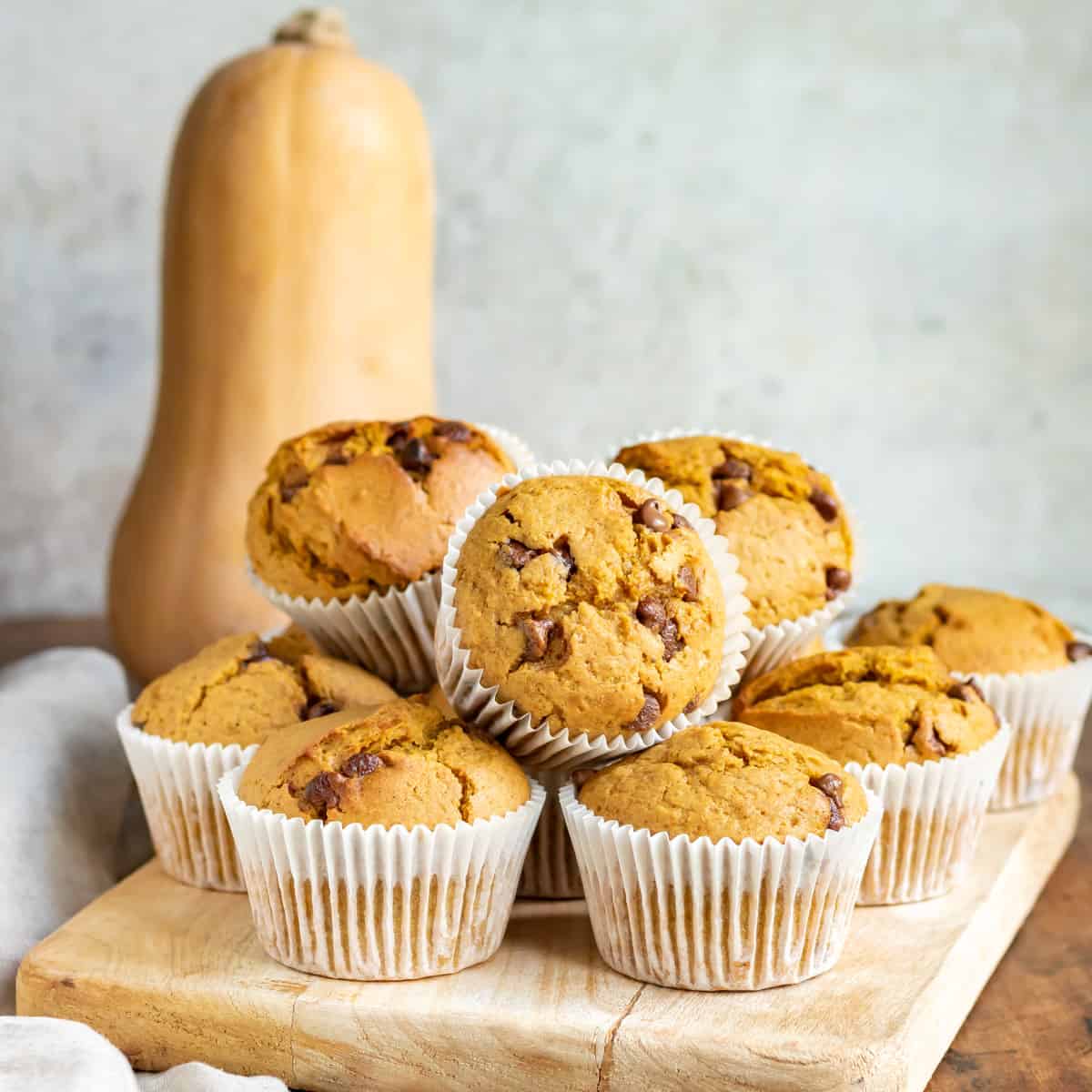 A pile of muffins in front of a butternut squash.