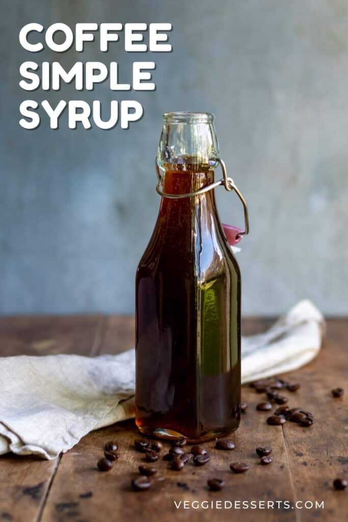 A bottle of syrup on a table with coffee beans, with text: coffee simple syrup.