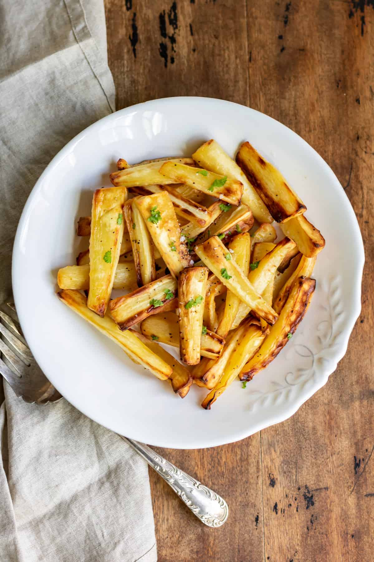 A wooden table with a plate of air fryer roasted parsnips.