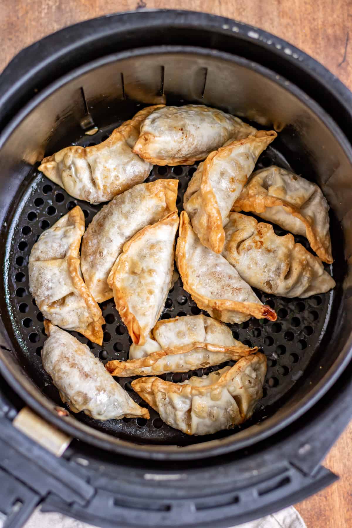 Cooked potstickers in the bowl of an air fryer.