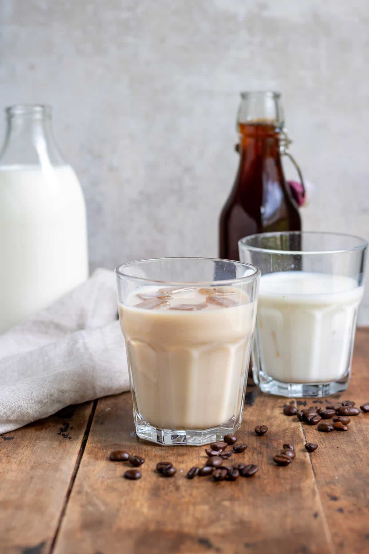 A table with a bottle of milk, bottle of coffee milk syrup and glasses of milk.