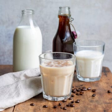 A table with a bottle of milk, bottle of coffee milk syrup and glasses of milk.