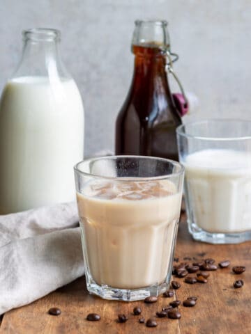 A table with a bottle of milk, bottle of coffee milk syrup and glasses of milk.