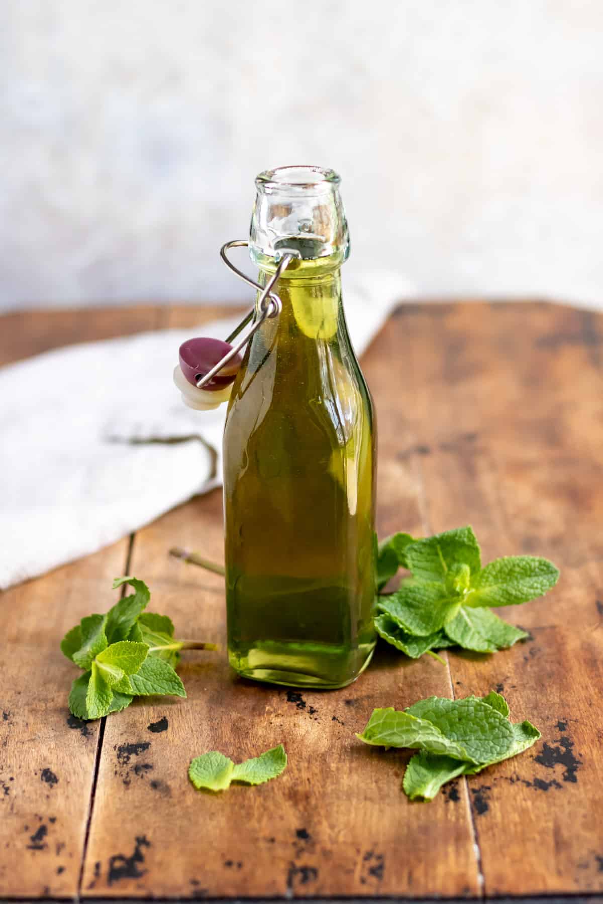 Wooden table with a bottle of syrup and sprigs of fresh mint.