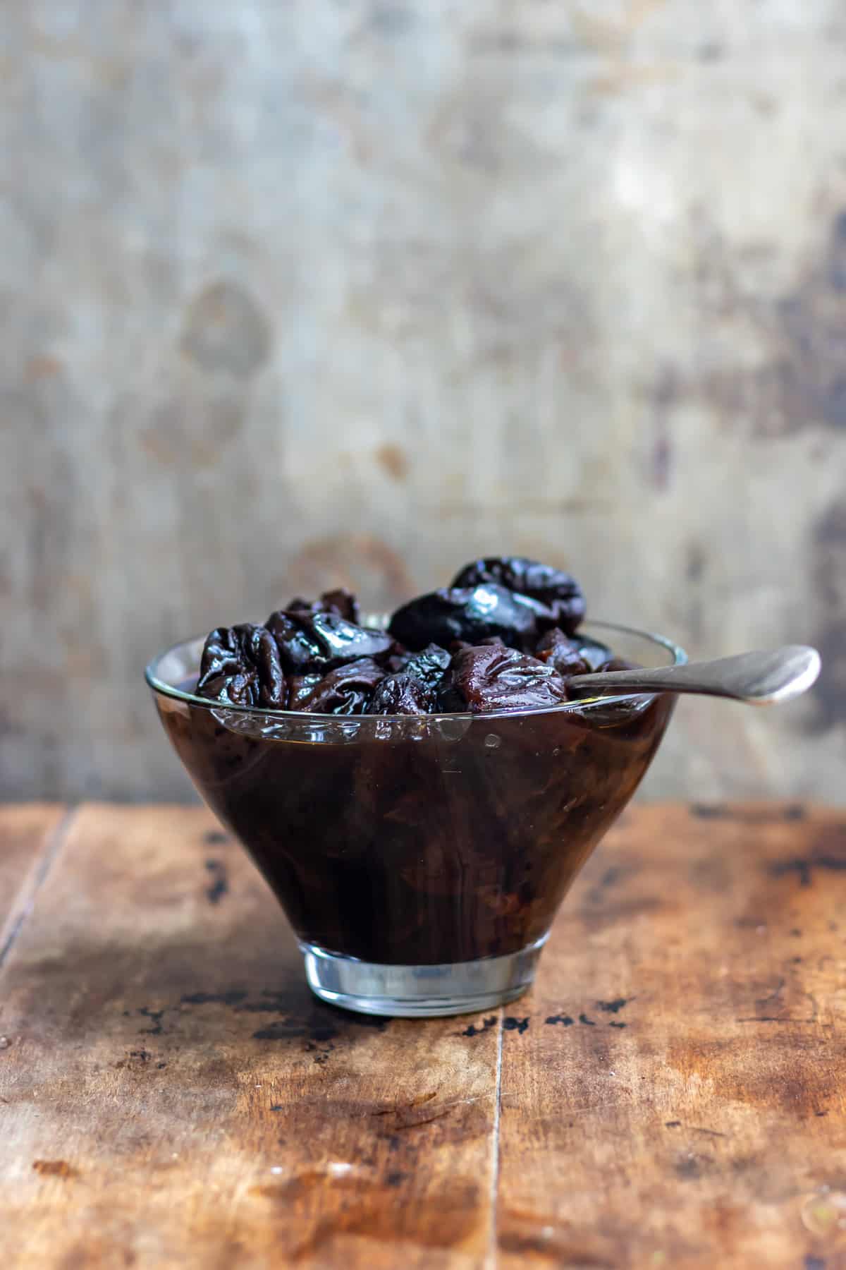 Dish of cooked prunes on a wooden table.