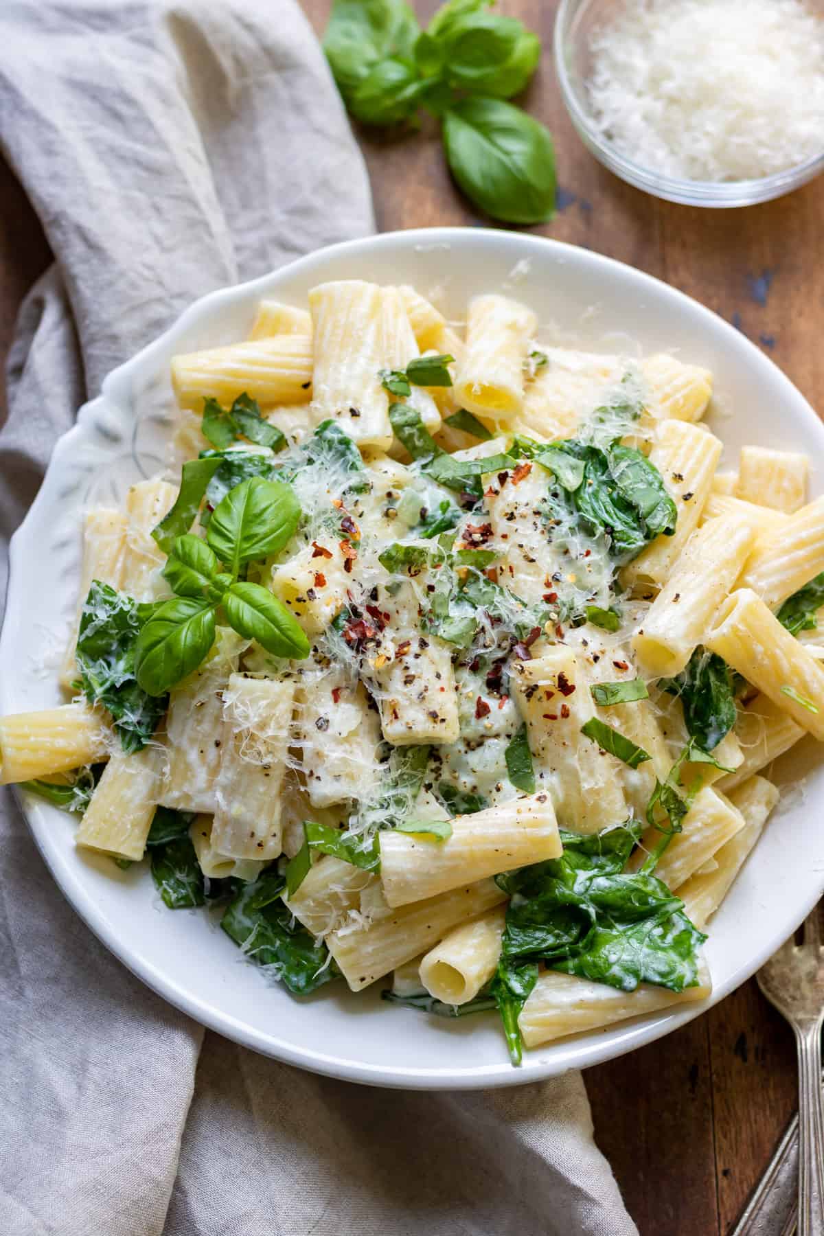 Table with a pasta full of spinach, goats cheese and topped with basil.