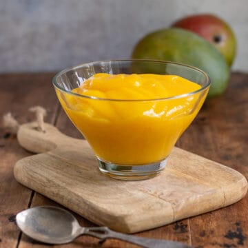 A bowl of pureed mango on a wooden board.