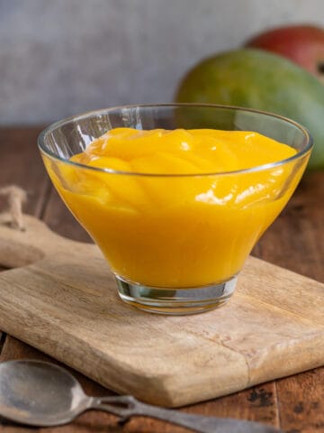 A bowl of pureed mango on a wooden board.