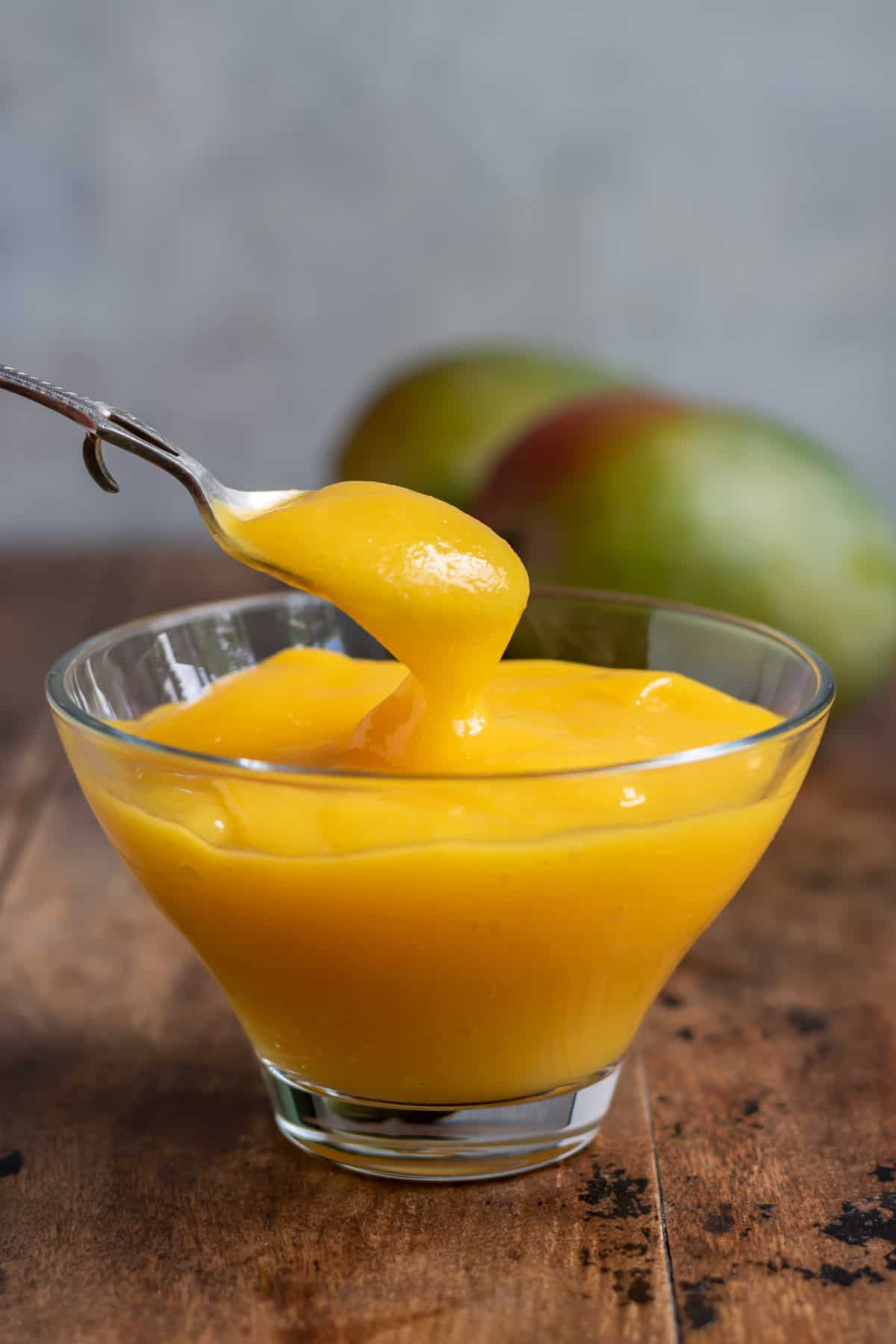 Spoon in a dish of mango pulp on a wooden table.