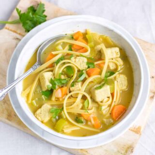 A table with a bowl of vegan chicken noodle soup.