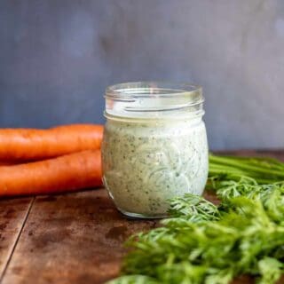 Table with a jar of salad dressing, next to carrots with carrot tops.