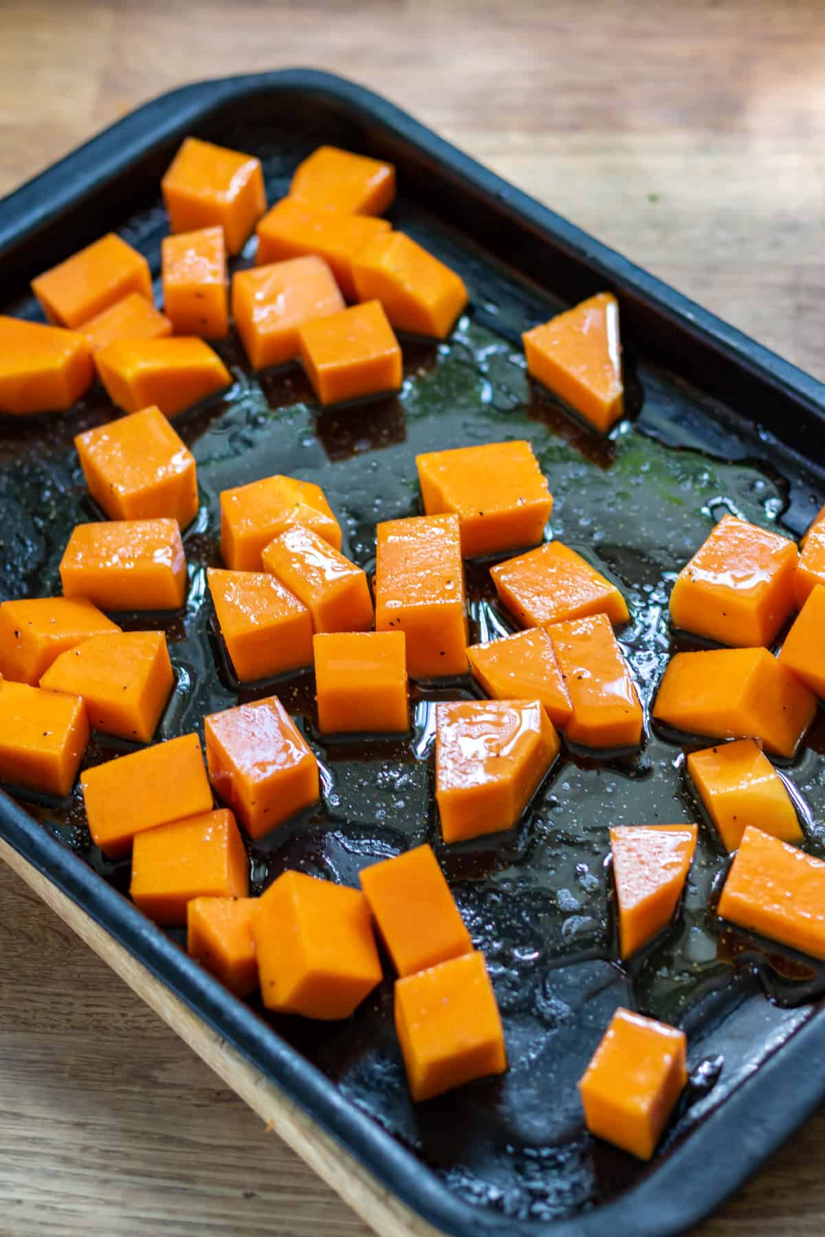 Drizzling cubes of squash with oil and seasonings.