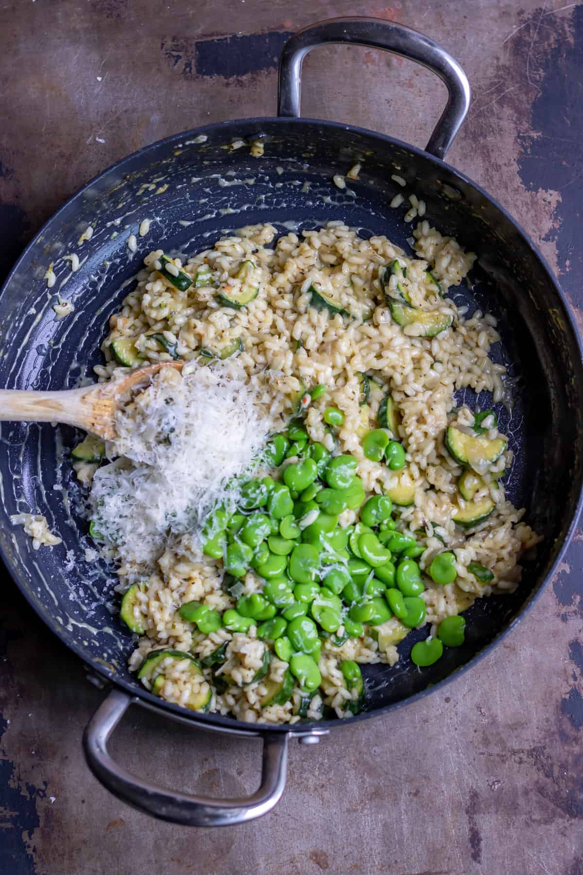 Adding parmesan and broad beans to the pan.