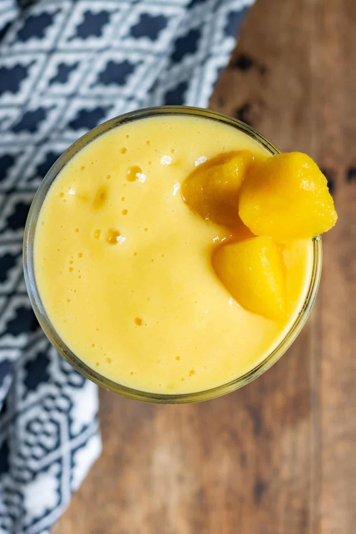 Looking down at a glass of smoothie with mango chunks to garnish.