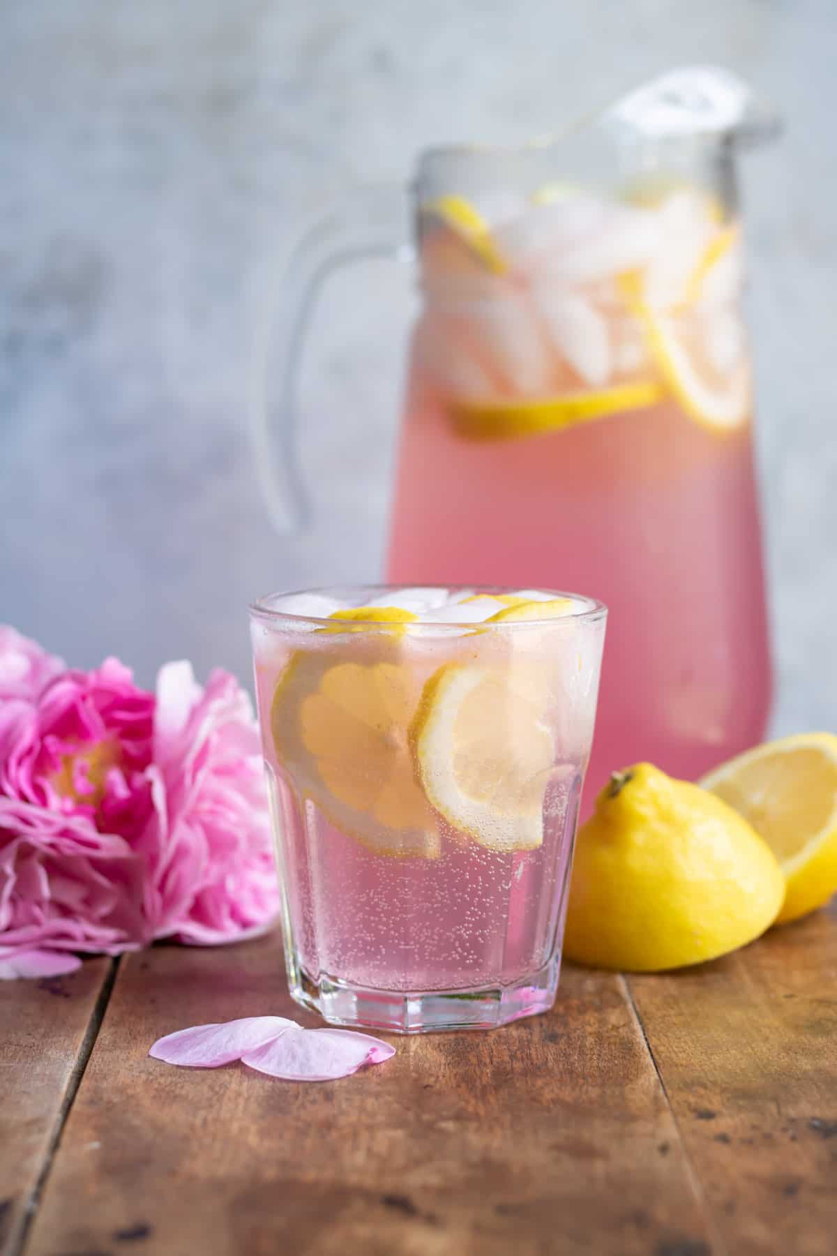 A glass of rose lemonade with ice and lemon slices.