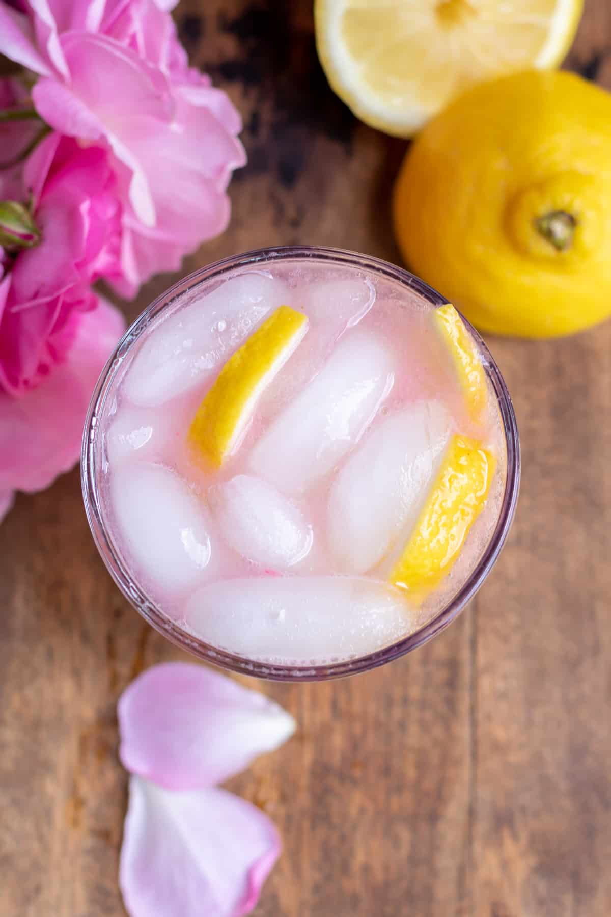 Looking down at a glass of rose lemonade, next to roses and lemons.